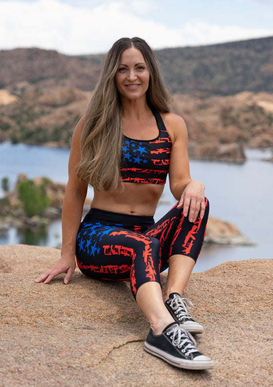 Woman wearing a patriotic set of activewear, capris and sports bra in black red and blue with gun flags of the USA and blue stars out on a hike in arizona by watson lake