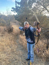 Woman shooting traditional archery with a bow and arrow and wearing a turkey feather hoodie from River to Ridge Clothing Brand