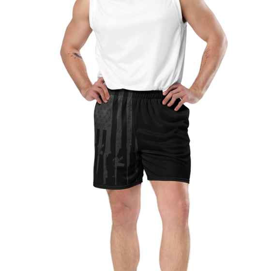 close up of a muscular man wearing gym shorts with a tactical gunmetal pattern on them in black for river to ridge brand and a white muscle tank