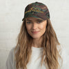 Product mockup of a Camo Low profile River to Ridge logo dad hat with curved visor worn by a young pretty blonde woman