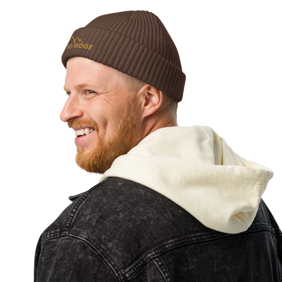 Product mockup of a fisherman's style skull cap beanie from River to Ridge Clothing Brand with the mountain logo on it worn by a man with a beard