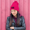 Hot Pink Knit Hat with pom pom and the River to Ridge R to R mountain logo stitched in black - worn by a woman in a leather jacket leaning up against a pink wall