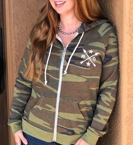 red haired woman wearing a camo zip up hoodie with rockstarlette arrow logo on it; sold by River to Ridge Clothing Brand