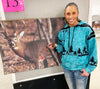 woman at an archery shoot for bowhunting who has shot a target of a deer with an arrow and she is wearing jeans and an archery themed hoodie in teal blue with black arrows and trees on it