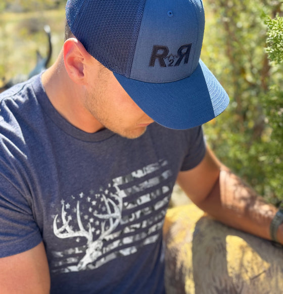 Guy pulling an arrow out of a 3D target wearing a Blue R2R Logo hat and a blue whitetail flag T shirt from River to Ridge Clothing Brand