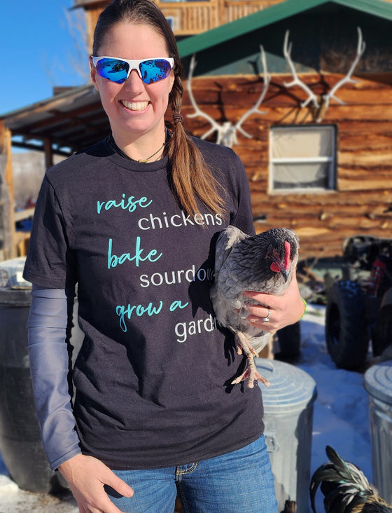 Women's T Shirt that says Raise Chickens, bake sourdough, grow a garden from the brand River to Ridge Clothing - worn by a woman holding a chicken