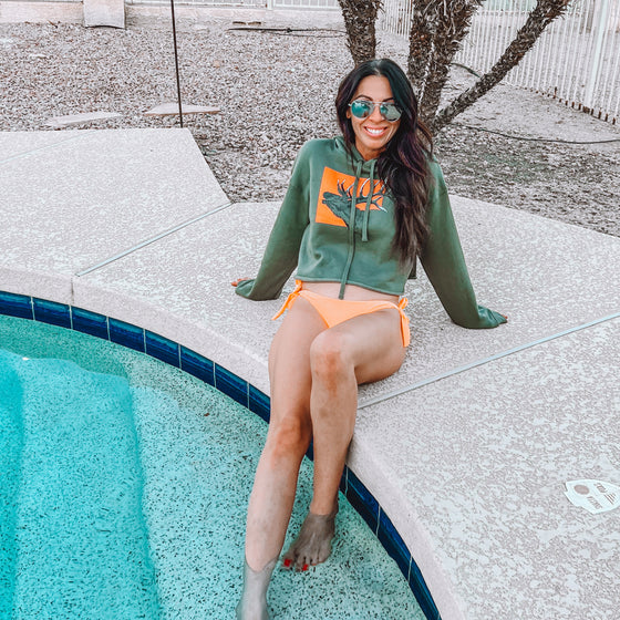 Woman at the pool on diving board wearing a River to Ridge brand cropped Elk Logo hoodie and bikini bottoms in green and orange