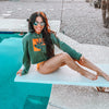 Woman at the pool on diving board wearing a River to Ridge brand cropped Elk Logo hoodie and bikini bottoms in green and orange