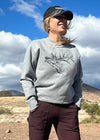 pretty woman standing on dirt road wearing elk sweatshirt, hat and work pants  from river to ridge clothing brand