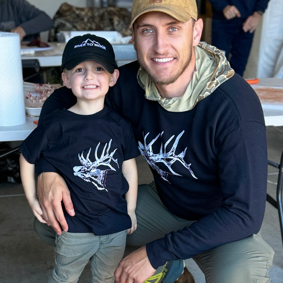 Kids River to Ridge Logo hat in black with our mountain logo stitched in white on a little boy with his dad