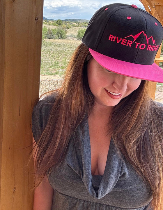 Woman wearing River to Ridge hot pink and black flatbill hat outside