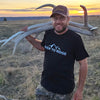 Men's River to Ridge Clothing brand Logo T shirt featuring the mountain logo in black and white worn by a man shed hunting for elk antlers with some on his shoulder