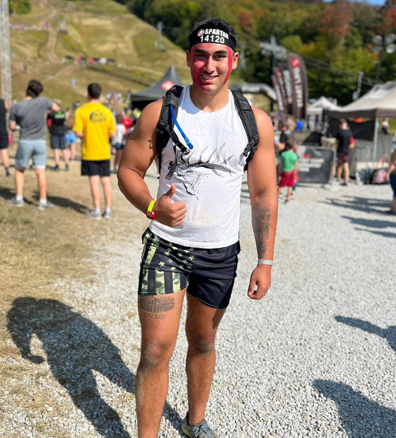 Man at  Spartan Obstacle Race wearing Mens Gym Shorts with Camo American Flag Pattern from River to Ridge Clothing Brand and also a white muscle tank top with an elk on it