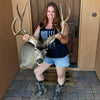 Womens tactical tank top in black with a grey USA flag made from guns and rifles and bullets from River to Ridge Clothing Brand - woman wearing the tank top and corral cowboy boots and holding up taxidermy of a large mule deer with big antlers