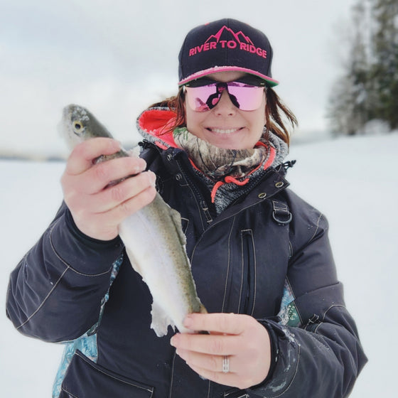 Woman wearing River to Ridge hot pink and black flatbill hat outside in the snow - ice fishing