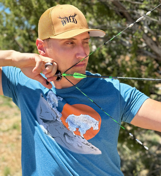 Man at full draw shooting a compound archery bow and wearing a WILD antler logo copper hat from River to Ridge Clothing Brand