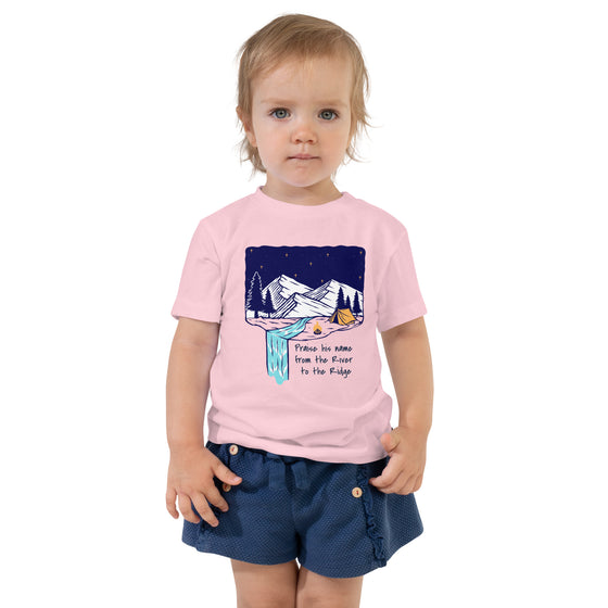 Product mockup of a Christian Scripture T shirt from River To Ridge clothing for children with a waterfall and camping tent on it