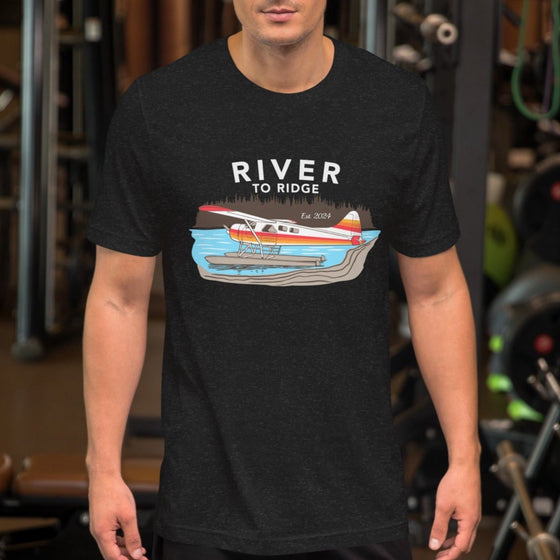 Man at the gym wearing an Alaskan bush plane shirt for fly in fishing on floats in the lake, t shirt is black heather. From the River to Ridge Brand - Backcountry Taxi