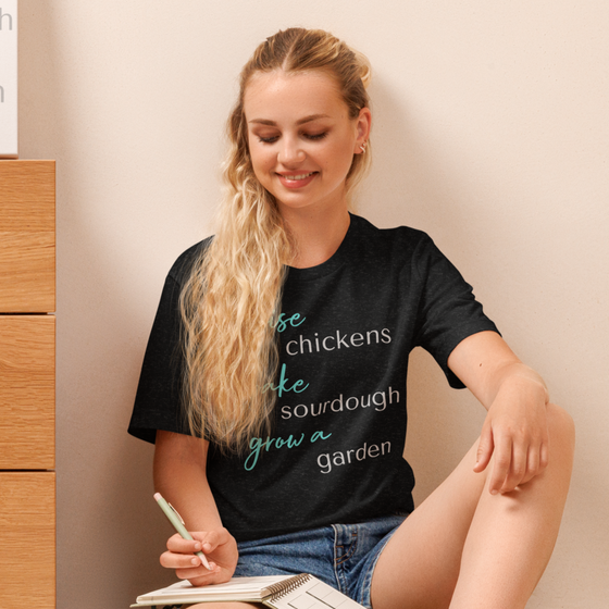 Women's T Shirt that says Raise Chickens, bake sourdough, grow a garden from the brand River to Ridge Clothing - worn by a woman writing in her journal