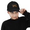 Kids WILD Logo hat from River to Ridge Brand. featuring the Stay Wild logo in gold stitching with elk antlers on the I and L. Photo of a little boy wearing black shirt and wearing the hat